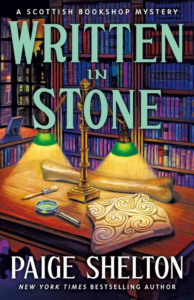 Cover of Written in Stone, showing a table in a library with desk lights shining on a bone, a carving, and a magnifying glass
