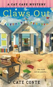 The cover of Claws Out shows a row of beach houses being used as book stalls with the ocean in the background and a cat on a book truck in the foreground.